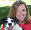 Bio photo of Shelly Thompson, smiling in a red shirt with her black and white dog, in a park setting